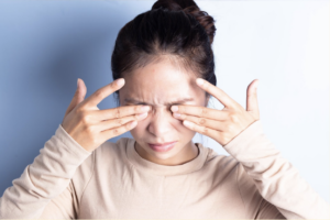 A young woman squinting and rubbing her eyes in discomfort.